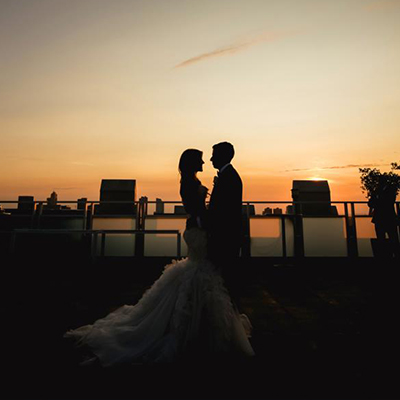 photo: bride and groom standong on rooftop with orange sunset in the background