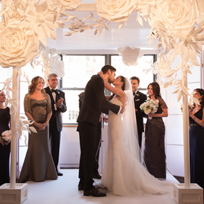 photo: bride and groom kissing under the chuppah decorated with large white paper flowers